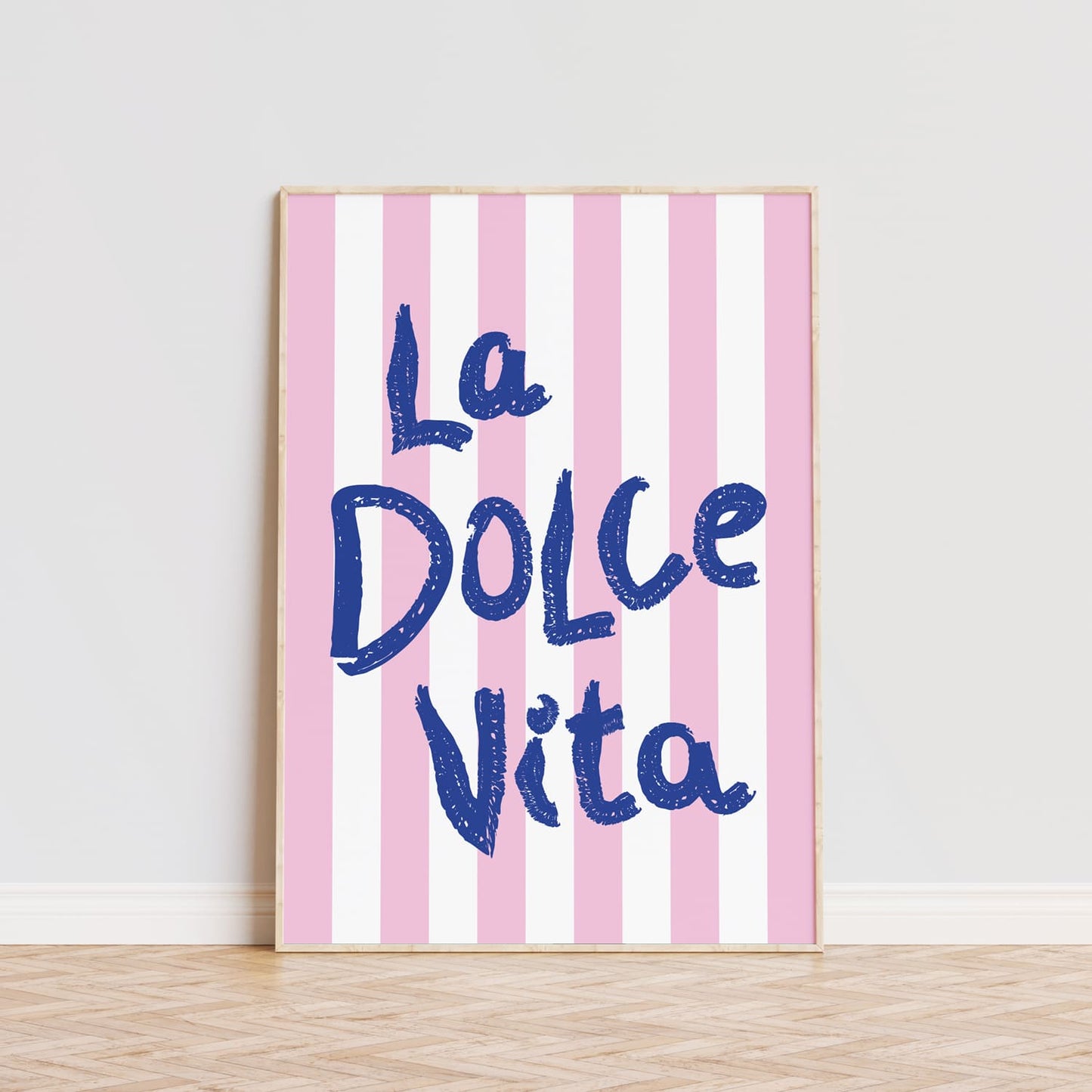 Póster decorativo personalizado con la frase 'La Dolce Vita' en letras grandes de color azul sobre un fondo de rayas verticales en tonos rosa y blanco. Este cuadro moderno es ideal para aportar un toque alegre y vibrante a cualquier habitación, comedor o cocina. La tipografía llamativa y el diseño sencillo lo convierten en una opción perfecta para quienes buscan decorar con estilo y personalidad. Lámina ideal para amantes de la decoración moderna que quieran añadir un detalle único y sofisticado a sus pared