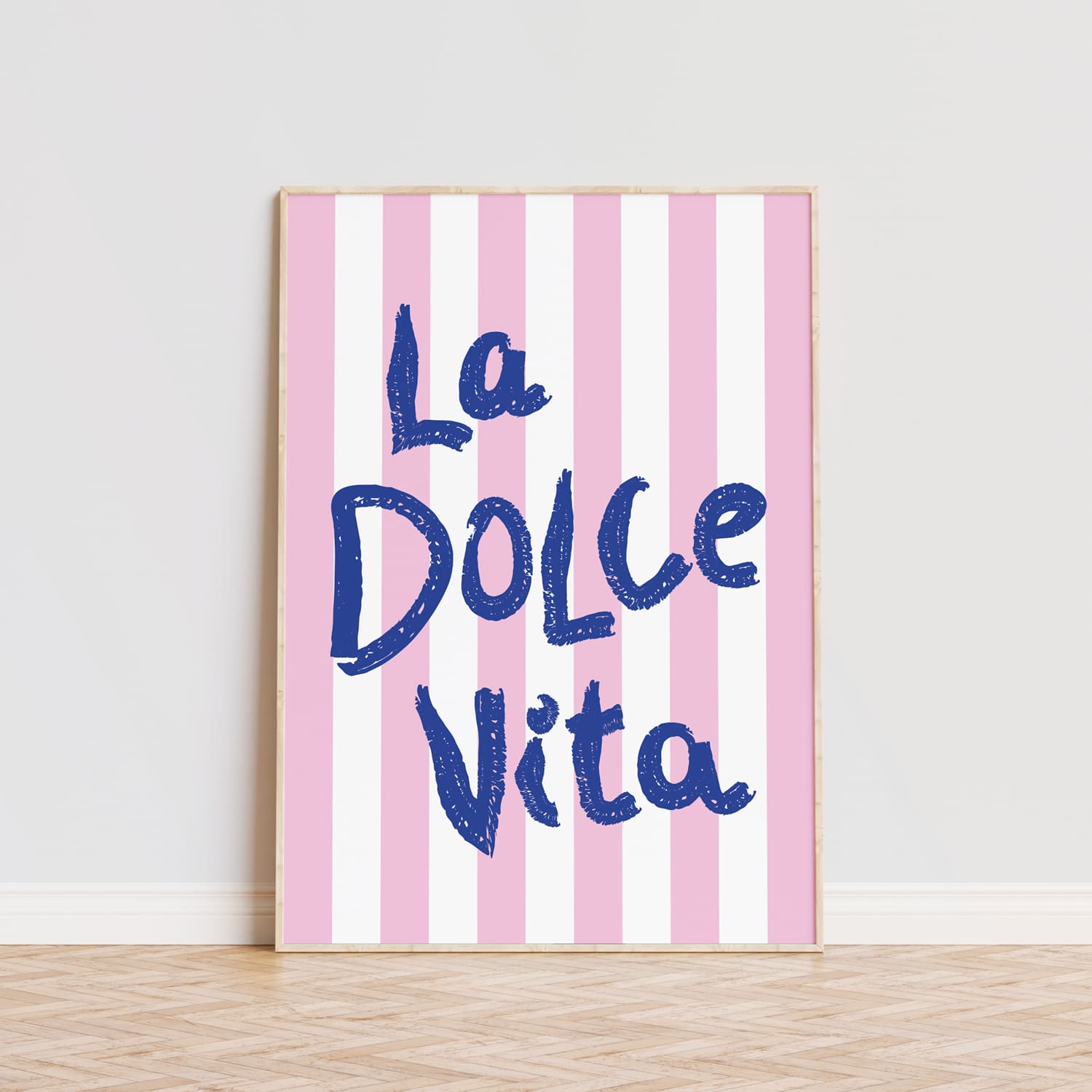 Póster decorativo personalizado con la frase 'La Dolce Vita' en letras grandes de color azul sobre un fondo de rayas verticales en tonos rosa y blanco. Este cuadro moderno es ideal para aportar un toque alegre y vibrante a cualquier habitación, comedor o cocina. La tipografía llamativa y el diseño sencillo lo convierten en una opción perfecta para quienes buscan decorar con estilo y personalidad. Lámina ideal para amantes de la decoración moderna que quieran añadir un detalle único y sofisticado a sus pared