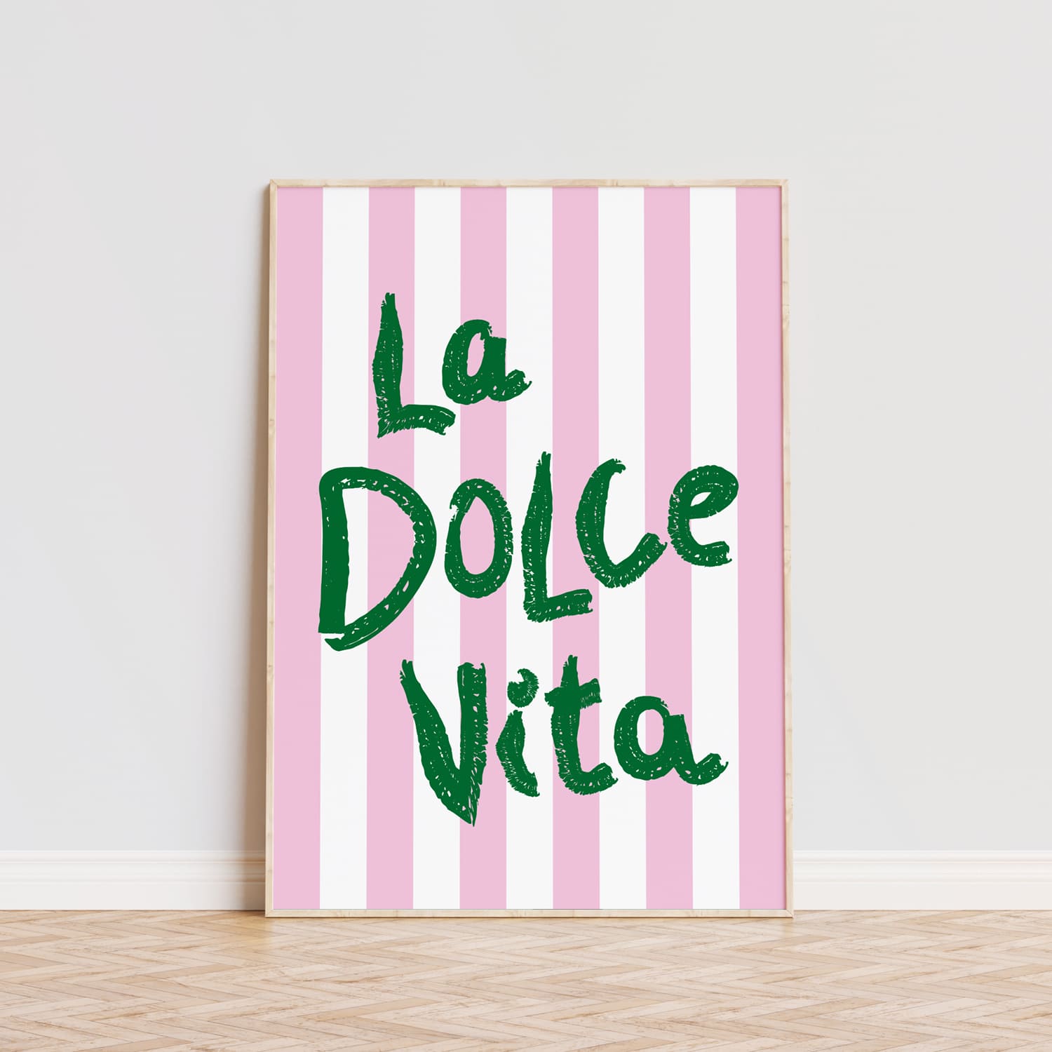 Póster decorativo con la frase 'La Dolce Vita' en letras grandes de color verde sobre un fondo de rayas verticales en tonos rosa y blanco. Este cuadro moderno es ideal para aportar un toque alegre y vibrante a cualquier habitación, comedor o cocina. La tipografía llamativa y el diseño sencillo lo convierten en una opción perfecta para quienes buscan decorar con estilo y personalidad. Lámina ideal para amantes de la decoración moderna que quieran añadir un detalle único y sofisticado a sus pared.