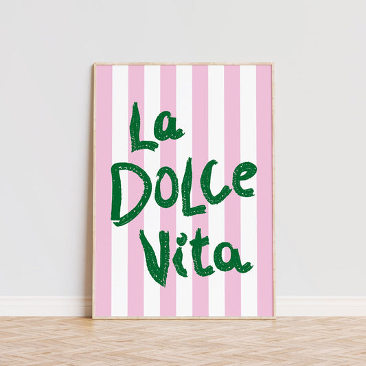 Póster decorativo con la frase 'La Dolce Vita' en letras grandes de color verde sobre un fondo de rayas verticales en tonos rosa y blanco. Este cuadro moderno es ideal para aportar un toque alegre y vibrante a cualquier habitación, comedor o cocina. La tipografía llamativa y el diseño sencillo lo convierten en una opción perfecta para quienes buscan decorar con estilo y personalidad. Lámina ideal para amantes de la decoración moderna que quieran añadir un detalle único y sofisticado a sus pared.