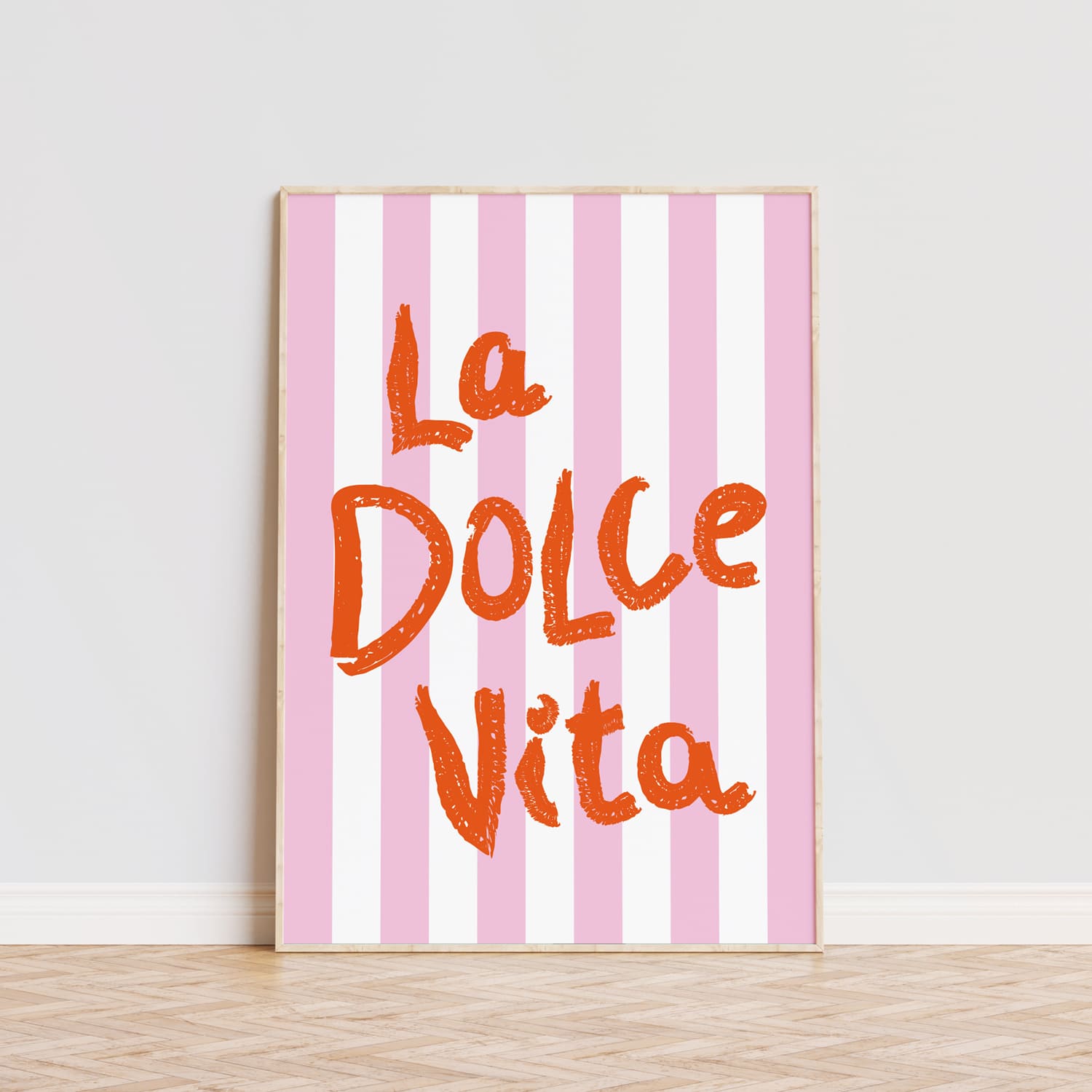 Póster decorativo con la frase 'La Dolce Vita' en letras grandes de color naranja sobre un fondo de rayas verticales en tonos rosa y blanco. Este cuadro moderno es ideal para aportar un toque alegre y vibrante a cualquier habitación, comedor o cocina. La tipografía llamativa y el diseño sencillo lo convierten en una opción perfecta para quienes buscan decorar con estilo y personalidad. Lámina ideal para amantes de la decoración moderna que quieran añadir un detalle único y sofisticado a sus pared